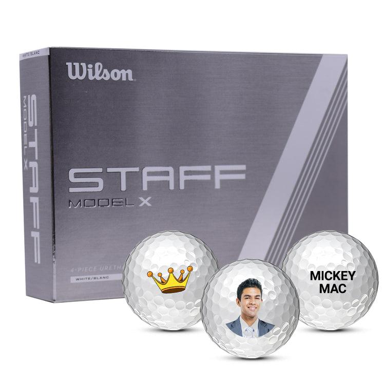 Box of Wilson Staff X golf balls with three custom golf balls in front of it. The left golf ball has an image of a crown, the center ball has a photo of a guy's face, and right ball has text that says MICKEY MAC.